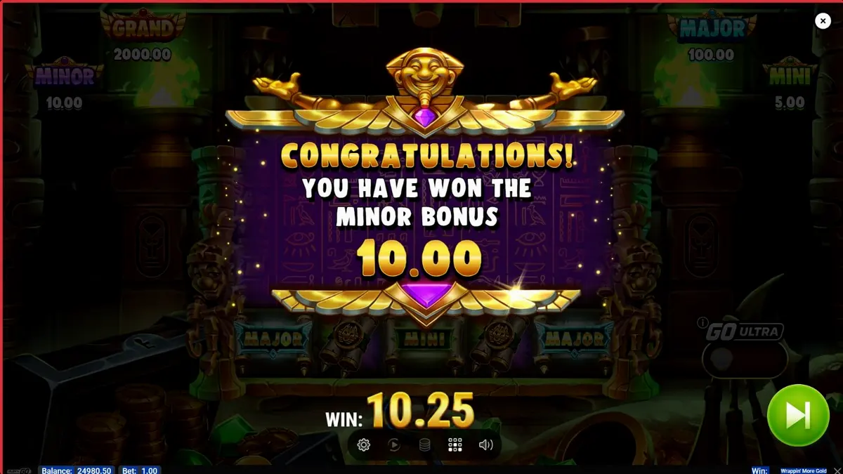 Mumi ramah dalam permainan slot Wrappin’ More Gold dengan latar belakang harta karun Mesir